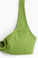 Top de bikini verde con textura, breteles anchos y anilla revestida en el centro del busto.