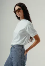 Camiseta blanca de algodón orgánico con cuello redondo alto y mangas cortas dobladas. Presenta un pequeño logo bordado en el pecho.