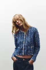 Chaqueta corta azul con tejido de punto entrelazado, cuello redondo, manga larga, bolsillos delanteros de plastrón y cierre frontal con botones dorados.