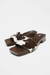 Sandalia tipo mule con estampado animal print en marrón y blanco, detalle de tachas plateadas en la suela y tacón bajo de bloque.