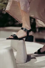 Sandalias de gamuza color marrón claro con tacón de madera. Presentan una correa ancha en la parte delantera con detalles de doble hebilla metálica plateada y una correa trasera ajustable mediante una hebilla adicional.