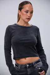 Remera negra de manga larga con efecto acid wash y cuello redondo decorado con tachas plateadas.