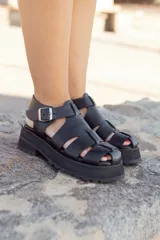 Sandalias negras de cuero con plataforma track y múltiples tiras anchas con aberturas en el empeine. Tira trasera con hebilla metálica ajustable.