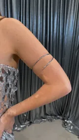 Brazalete plateado de metal con diseño de doble aro abierto.