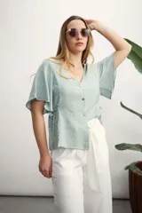 Camisa color verde agua con escote en V, cierre frontal con botones y mangas cortas con volados. Ajuste en la cintura con lazos laterales.