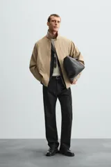 Parka ligera color beige, de corte relaxed fit, confeccionada en tejido técnico repelente al agua. Tiene cuello alto, mangas largas con puños ajustables con botón a presión, bolsillos de solapa en la cadera y cierre frontal con cremallera oculta por solapa con botones a presión.