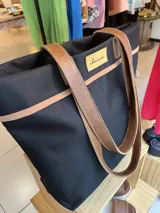 Bolso de lona color negro con detalles en cuero marrón, con bolsillo interno y forro de tela.