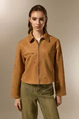 Campera cropped color camel de poliéster, con cuello camisero, cierre frontal y un bolsillo con cierre en el pecho. Está decorada con tachas plateadas distribuidas por toda la prenda.