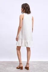 Vestido corto sin mangas, color celeste claro, con escote en V y un pequeño broche decorativo en la abertura frontal. Presenta un corte holgado tipo babydoll con bolsillos laterales y un ruedo con volado.