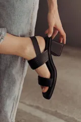 Sandalia de cuero color negro con taco bloque medio y punta cuadrada. Presenta dos tiras anchas sobre el empeine, una de ellas con hebilla metálica dorada, y una tira de sujeción en el talón. Posee base acolchonada para mayor comodidad.