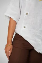 Blusa blanca de lino con corte asimétrico, mangas 3/4 con botones y cuello redondo amplio.