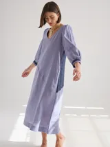 Vestido midi de lino color lila con escote en V y mangas 3/4 abullonadas con puño elástico. Presenta paneles laterales en denim y costuras a la vista en color rojo.