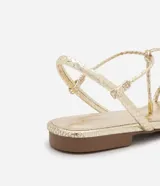 Sandalia plana marca Satinato, color dorado metalizado con textura tipo croco. Posee tiras finas con detalle de nudo en el empeine y cierre de lazo ajustable al tobillo. Diseño de puntera redonda y suela plana.