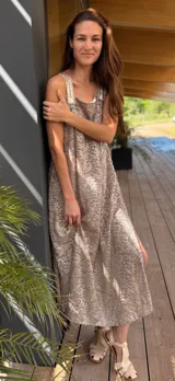 Vestido largo de tela metálica bordada color dorado, de corte suelto, con tajos laterales y breteles artesanales de cuero a tono.