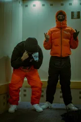 Campera puffer naranja con capucha desmontable y mangas desmontables, con logo reflectivo en el pecho.