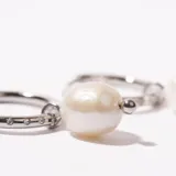 Aros tipo argolla plateados con incrustaciones de strass y dije colgante de perla irregular con bolita metálica.