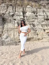 Conjunto de dos piezas color blanco, compuesto por un top corto con escote Bardot (hombros descubiertos) y una falda midi ajustada con textura fruncida (bambula elastizada).