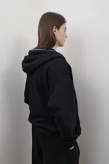 Campera negra con capucha, cierre metálico frontal, bolsillos laterales y corte oversize unisex.