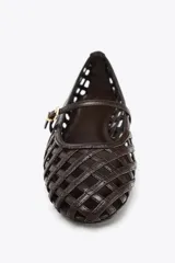 Zapato plano tipo bailarina color marrón oscuro, con capellada trenzada y tira delantera con hebilla metálica. Suela plana de 1 cm de altura y punta redonda.