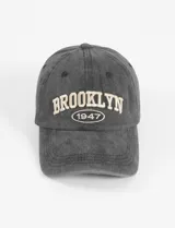 Gorra de béisbol gris gastada con bordado frontal de la palabra "Brooklyn" en color crema y el año "1947" debajo.