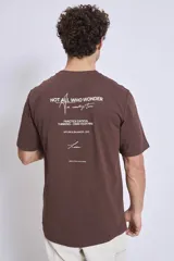 Remera de manga corta color marrón oscuro con cuello redondo y un pequeño texto bordado en blanco en el pecho.