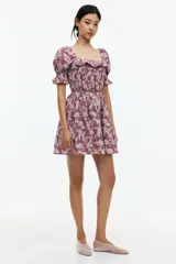 Vestido corto color lila con estampado floral en blanco, escote cuadrado con volados, mangas cortas abullonadas con elástico y cuerpo fruncido.