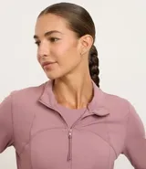 Campera deportiva de manga larga color malva o rosa viejo, con cuello alto y cierre frontal. Presenta recortes y costuras visibles que definen la silueta.