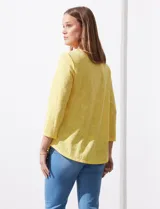 Blusa blanca de tejido labrado con cuello redondo, escote en V y aplique metálico.
