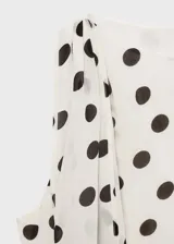 Blusa sin mangas color crema con estampado de lunares marrones, cuello alto con detalle de pañuelo y cierre de botón en la parte posterior.