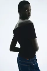 Top negro con textura, corte ajustado y escote off-the-shoulder con volantes.