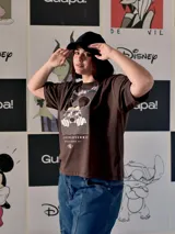 Remera marrón de manga corta y corte holgado, con estampado frontal de Mickey Mouse usando gafas de sol sobre un fondo de líneas onduladas y el texto "ALWAYS ON VACAY".