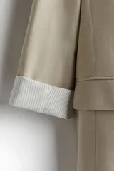 Blazer color beige de corte recto, con solapas de pico, bolsillos delanteros con solapa y mangas con forro a rayas.