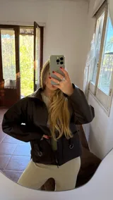 Campera corta de ecocuero marrón oscuro con cierre frontal y dos bolsillos con argollas decorativas.