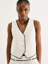 Chaleco blanco con ribete negro, cuello en V y cierre frontal con botones.