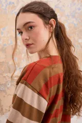 Blusa estilo remera de manga tres cuartos con corte recto y diseño a rayas horizontales en tonos marrón, naranja y beige.