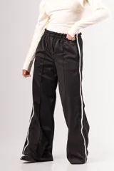 Pantalón negro de tela deportiva con cintura elástica ancha y cordón ajustable. Presenta corte amplio, bolsillos laterales y una franja blanca vertical a lo largo de cada pierna.