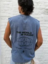 Musculosa sin mangas, color azul desgastado (acid wash), con estampado gráfico en la espalda que incluye el texto "OSTEN THE WORLD IS YOURS KEEP MOVING KEEP DREAMING" y un diseño de elipses entrelazadas.