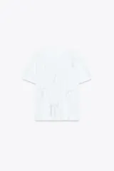 Camiseta blanca de algodón con cuello redondo, manga corta y apliques de lazos de raso blancos en el frente.