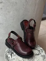 Zueco de cuero vacuno color bordó, con forrería vacuna, detalle de herrajes oro viejo y estribo. Tiene un taco de 4,5 cm y suela de goma.