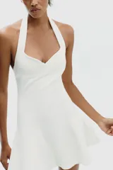 Vestido corto blanco de tejido de punto elástico, con cuello halter, escote corazón y cierre con botones en el cuello.