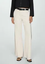 Pantalón de vestir color crema, de corte wide leg y tiro alto. Presenta trabillas para cinturón, bolsillos laterales y raya lateral negra.