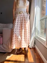 Falda midi de corte evasé con estampado de círculos color rosa y blanco. Incluye cinturón de cuero sintético color crema con hebilla dorada y bolsillos laterales.