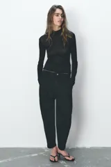 Pantalón de jean negro con efecto lavado, tiro alto, corte carrot fit, cintura elástica en la parte trasera, bolsillos delanteros y traseros, cierre frontal con cremallera y botón metálico.