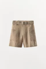 Bermuda color beige de lino, con cintura elástica, trabillas y cinturón con hebilla metálica. Presenta bolsillos de parche laterales y traseros.
