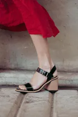 Sandalias de cuero charol negro con tira delantera y tobillera con hebilla metálica. Taco de madera con forma geométrica.