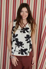 Top sin mangas de color blanco con escote en V y diseño holgado. Presenta un estampado artístico frontal en tonos azul y rojo, con terminaciones de vivo a contratono en color marrón.