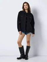 Chaqueta de jean negra de corte oversize, con cuello clásico, cierre frontal con botones metálicos, bolsillos delanteros con solapa y botón, y mangas largas.