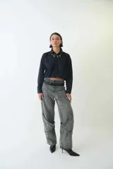 Pantalón jean gris de tiro medio con calce amplio, bolsillos delanteros y traseros, recortes en las piernas, trabillas para cinturón y cierre con botón y cremallera.