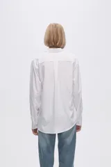 Camisa blanca de manga larga con cuello clásico y cierre frontal con botones. Corte recto y holgado.