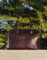 Bolso tipo tote de cuero negro con textura tipo piel de cocodrilo, doble asa de mano y cierre superior con cremallera.